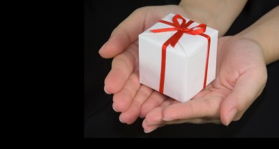 small white box wrapped with red ribbon in palm of hands