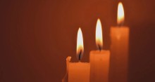 Three lighted white candles with a golden brown background.