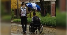 Man walking in rain holding umbrella over companion in wheelchair