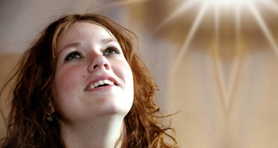 young woman looking up with light shining through church window in background