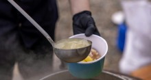 Person serving hot soup outdoors with ladle.